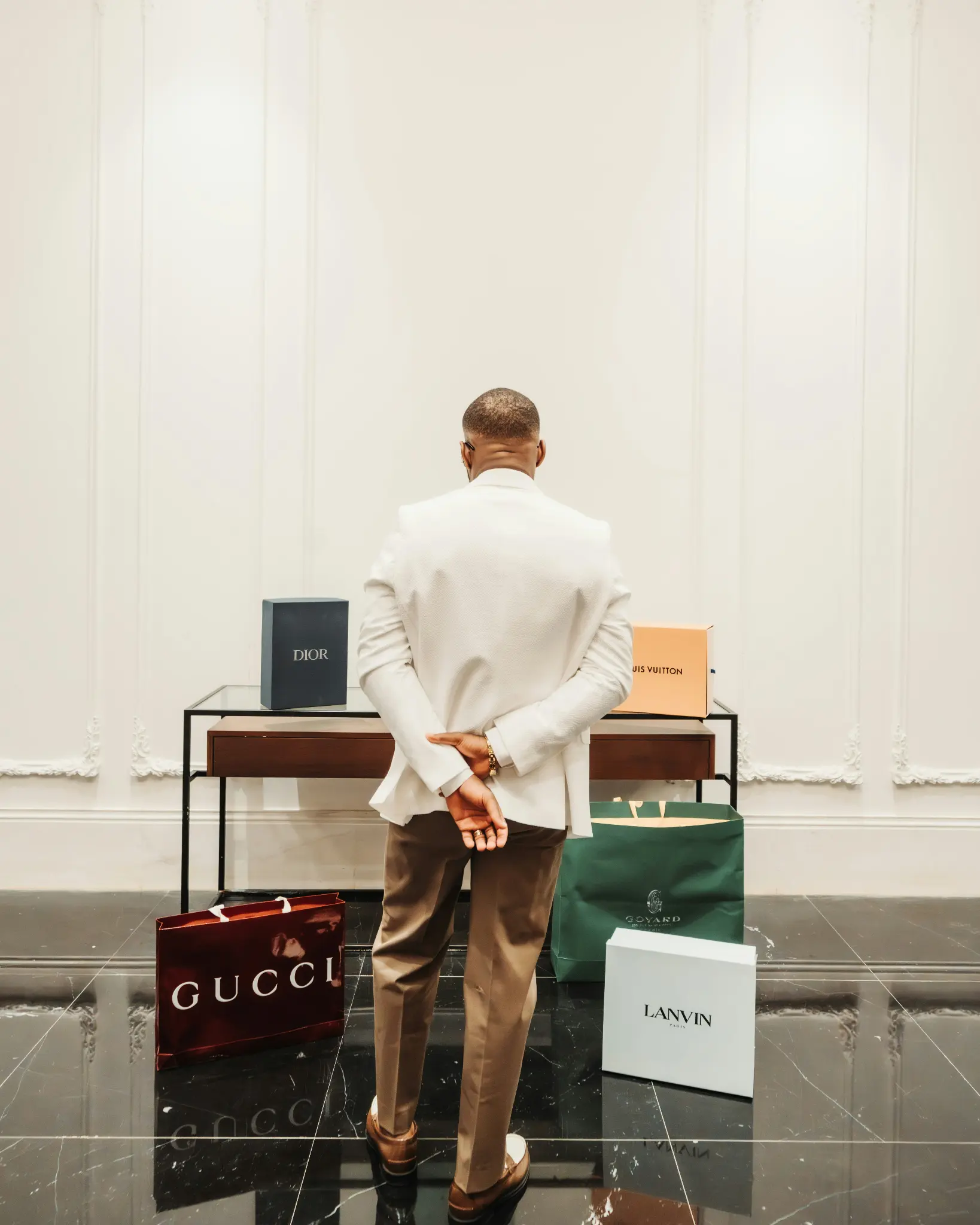 A man in a white jacket beside luxury shopping bags